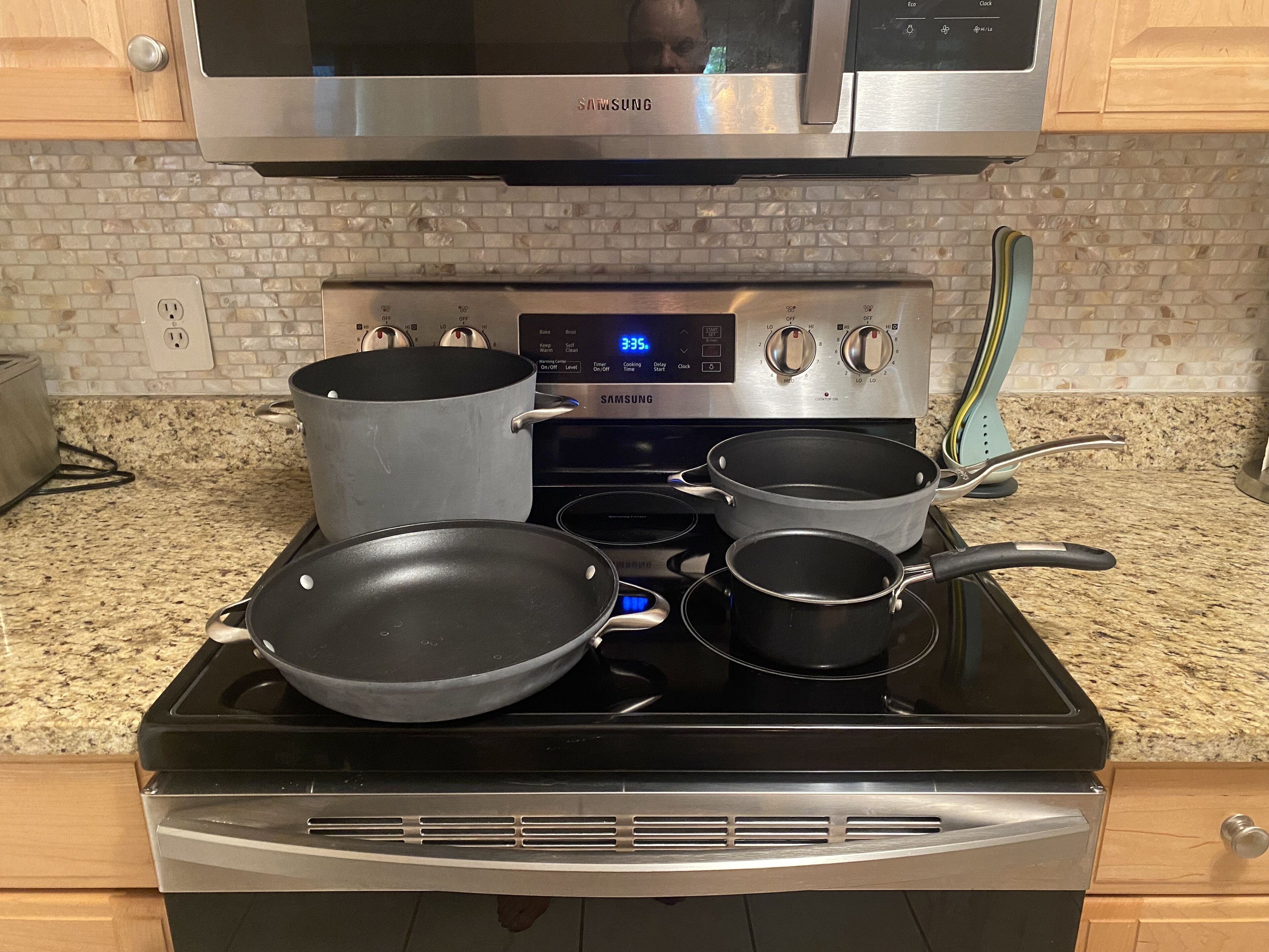 Una cucina con un piano cottura in acciaio inox, diverse pentole e padelle e un forno a microonde sopra.