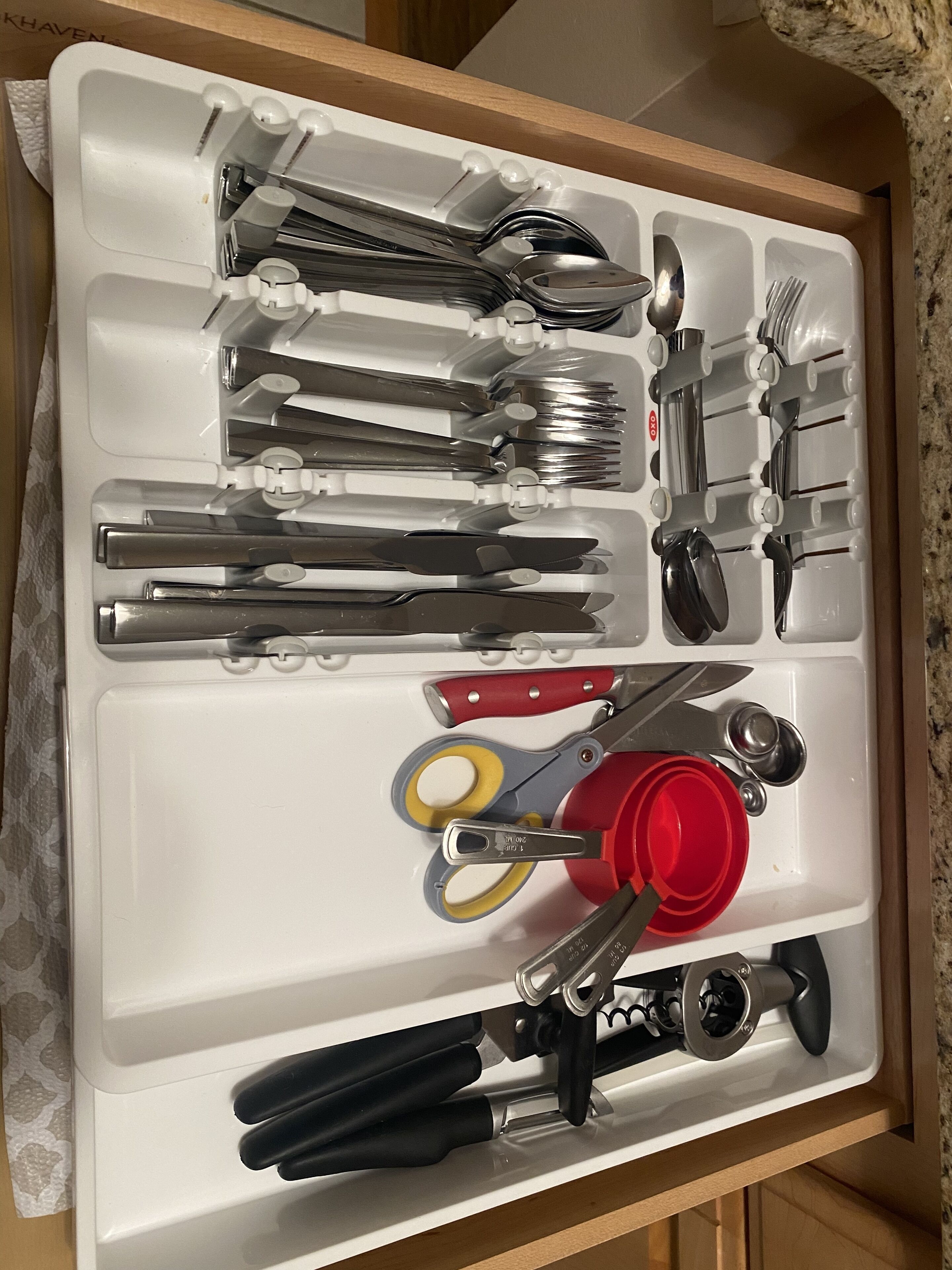 Un tiroir contenant divers ustensiles et outils de cuisine, notamment des couteaux, des ciseaux et des tasses à mesurer.