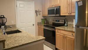 Una cocina con encimeras de granito, electrodomésticos de acero inoxidable, armarios de madera y una puerta blanca.