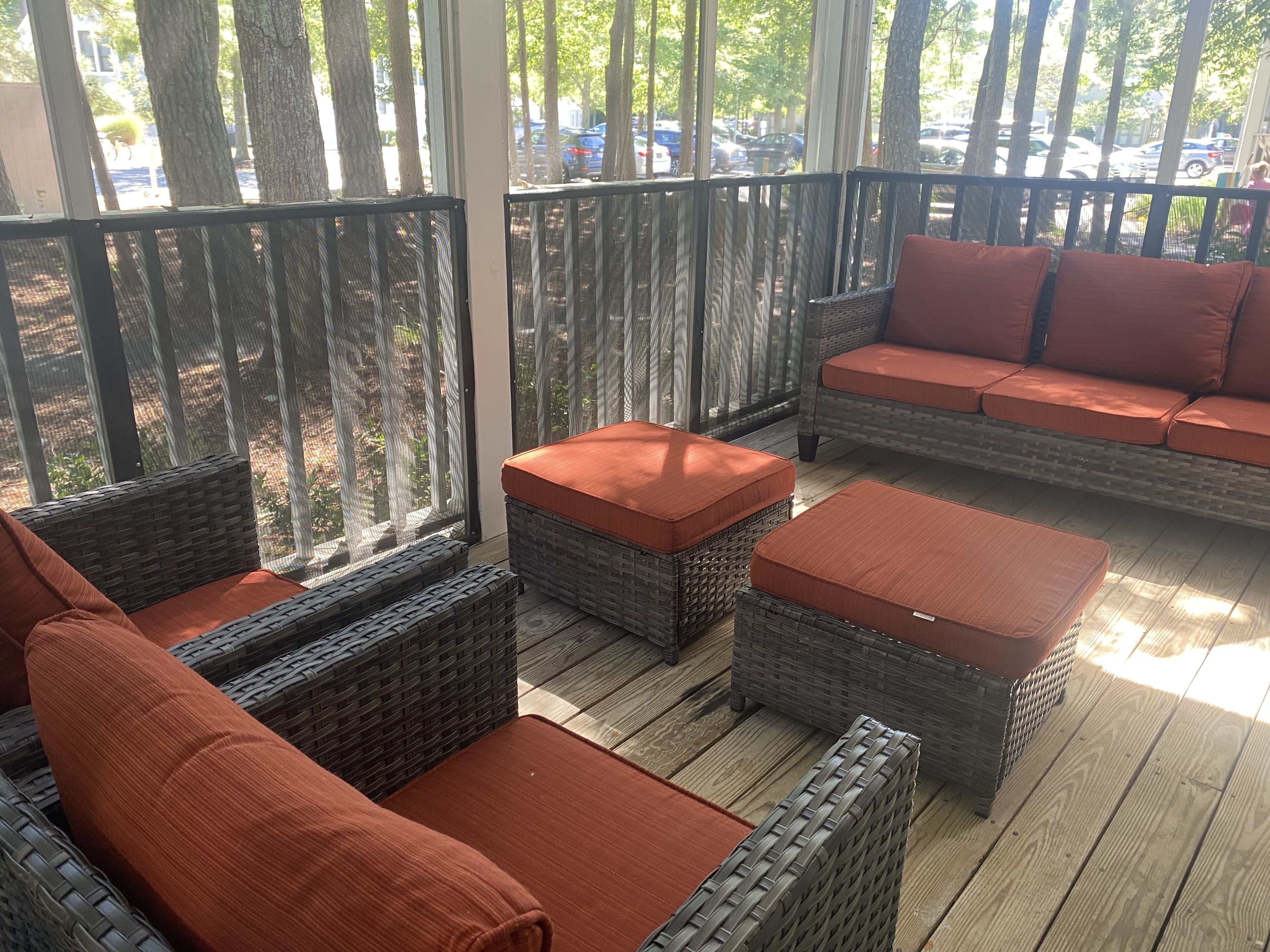 A covered outdoor seating area with wicker furniture and orange cushions, overlooking a parking lot.
