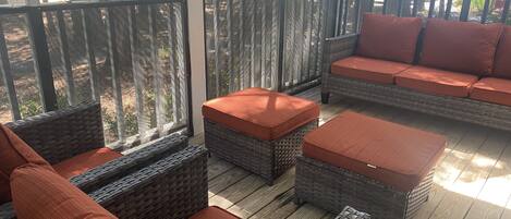 A covered outdoor seating area with wicker furniture and orange cushions, overlooking a parking lot.