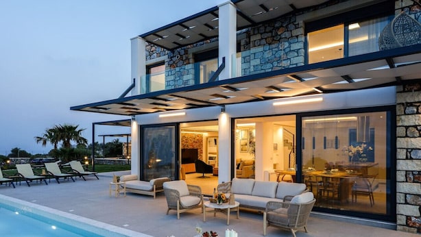 A modern two-story house with a pool, outdoor seating, and a stone facade. - Villa Empire Ultimate Luxury villa with heated pool (Kefalas)