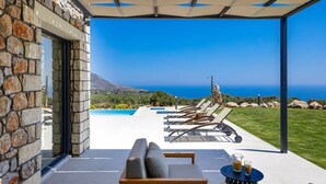 A modern outdoor seating area with a pool, stone walls, and a view of the sea. - Villa Empire Ultimate Luxury villa with heated pool (Kefalas)