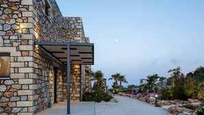 A modern building with a stone facade, outdoor seating area, and a gravel path with plants. - Villa Empire Ultimate Luxury villa with heated pool (Kefalas)
