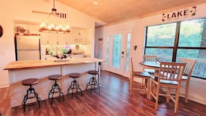 Una cocina con barra, taburetes de madera, una mesa de comedor con sillas y vistas a un lago.