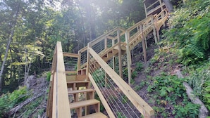 Una escalera de madera que asciende por una colina, rodeada de abundante vegetación y árboles.