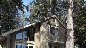 A two-story wooden house with large windows, a covered porch, and a concrete driveway.