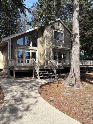 A two-story wooden house with large windows, a covered porch, and a concrete driveway.