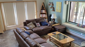 A spacious living room with a large brown leather sectional sofa, a wooden coffee table, and a bookshelf filled with books.