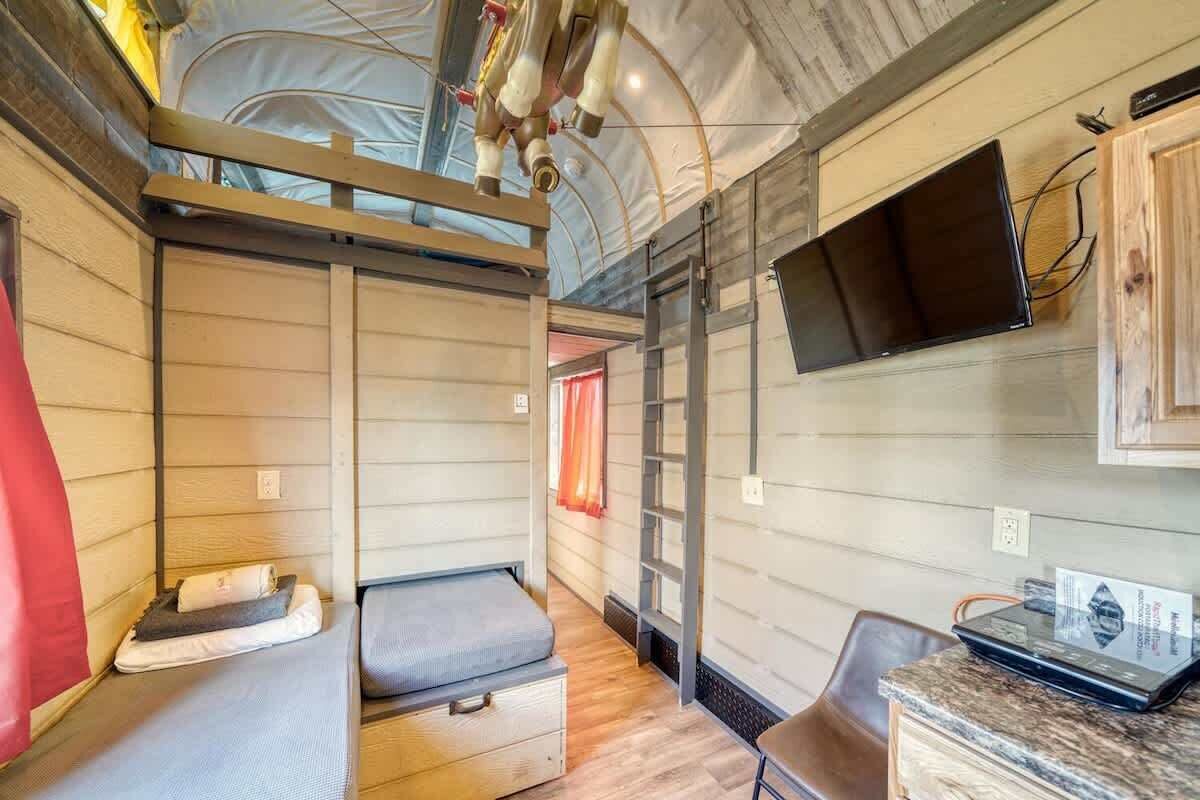 Kompakt autocamper indretning med to soveområder, et lille tekøkken og et monteret fjernsyn.