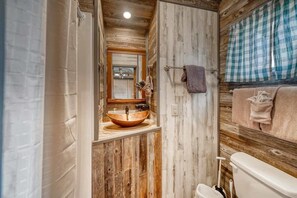 A rustic bathroom with a wooden vanity, a large mirror, and a toilet.