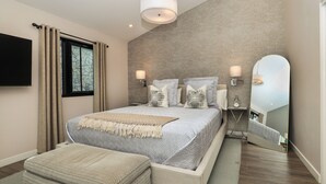 A modern bedroom with a large bed, bedside lamps, a mirror, and a television.