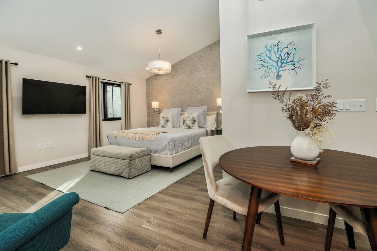 A modern bedroom with a bed, bedside lamps, a flat-screen TV, and a dining area with a table and chairs.