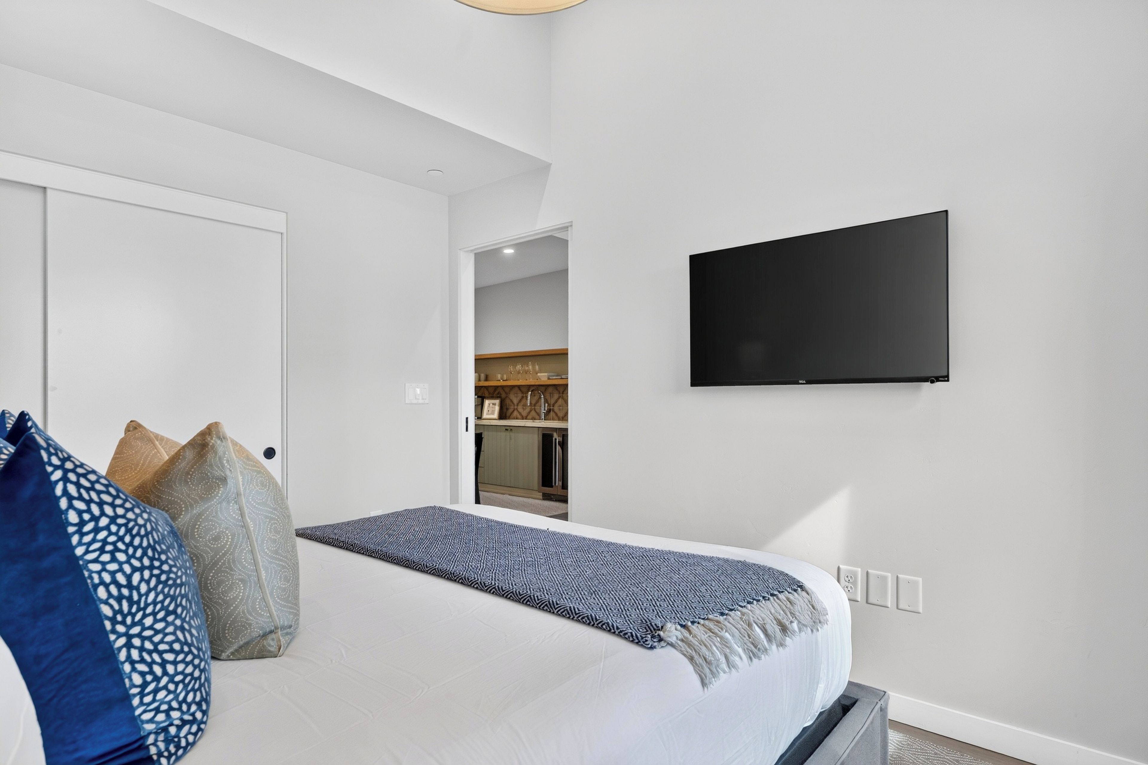 Habitación de hotel con cama, almohadas, un televisor montado en la pared y vistas al área de la cocina.