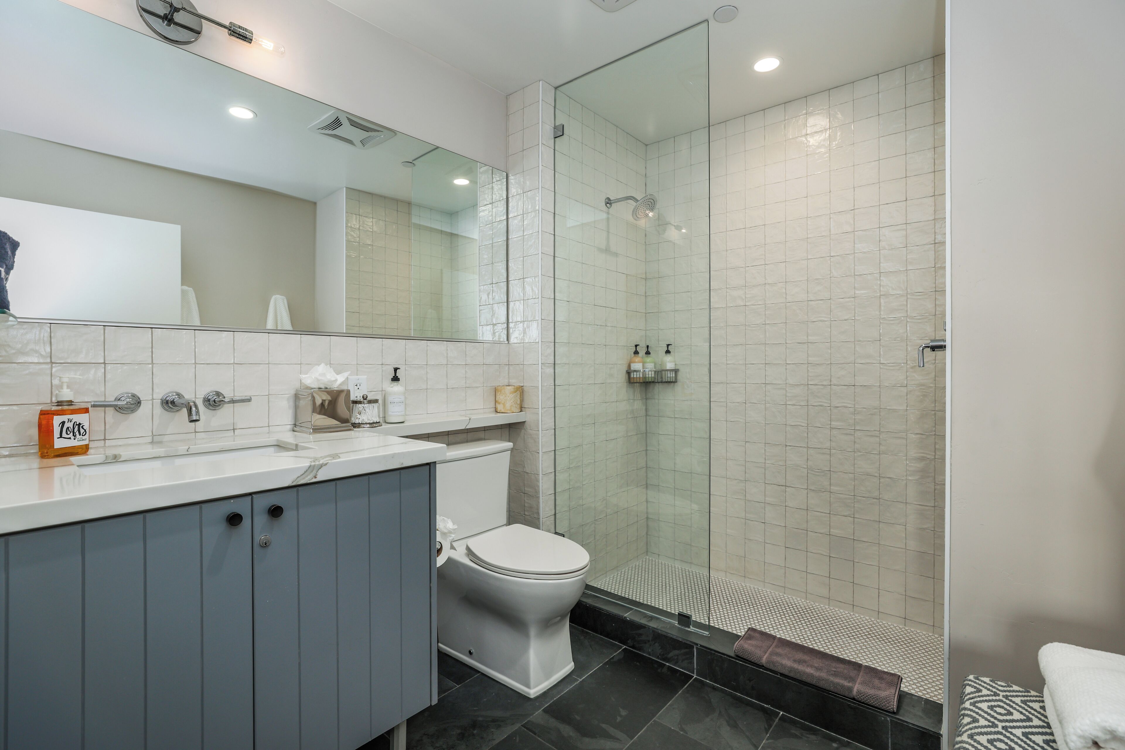A modern bathroom with a glass-enclosed shower, a white toilet, and a vanity with a mirror.