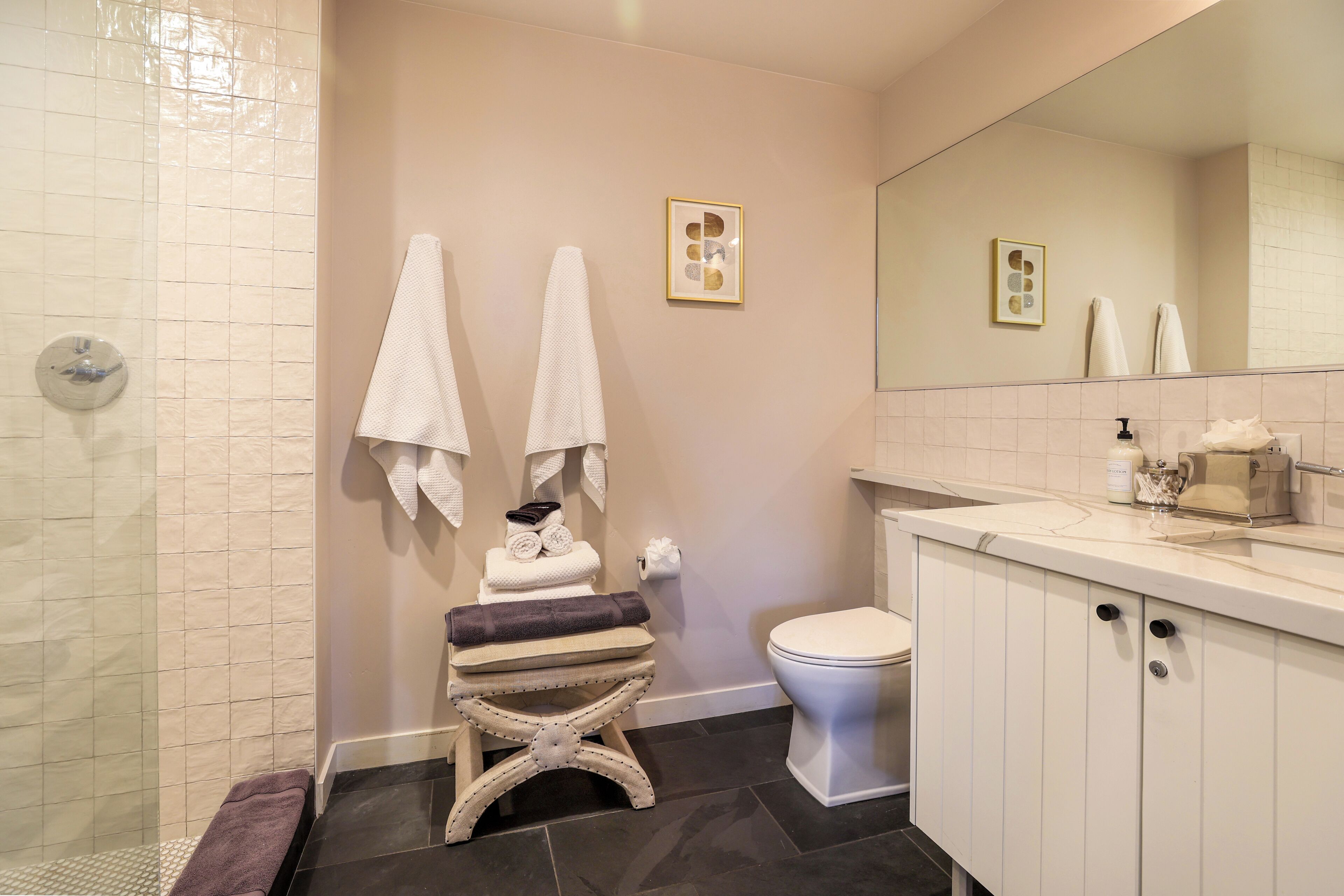 A bathroom with a shower, a toilet, a sink with a mirror, and two towels hanging on the wall.