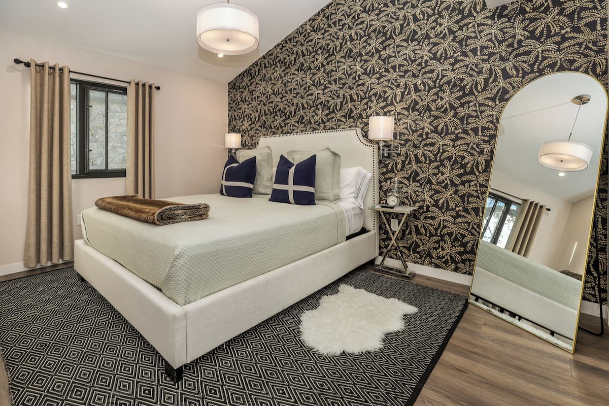 A bedroom with a large bed, a mirror, and patterned wallpaper.
