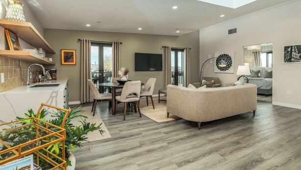 A spacious living area with a high ceiling, a dining table with chairs, a sofa, and a TV mounted on the wall.