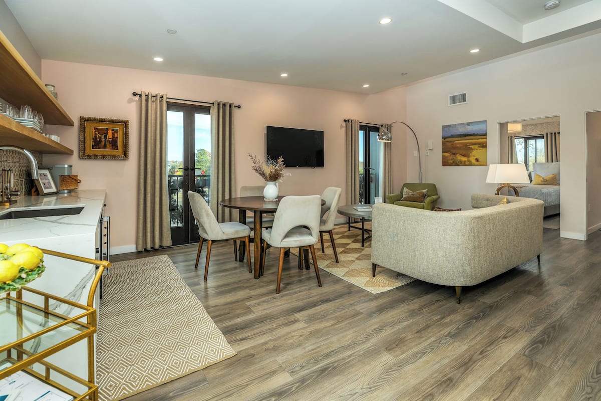 A modern living room with a dining area, a sofa, a TV, and a balcony with curtains.