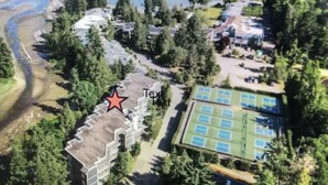 An aerial view of a residential area with a large building marked with a red star, surrounded by trees and a tennis court.