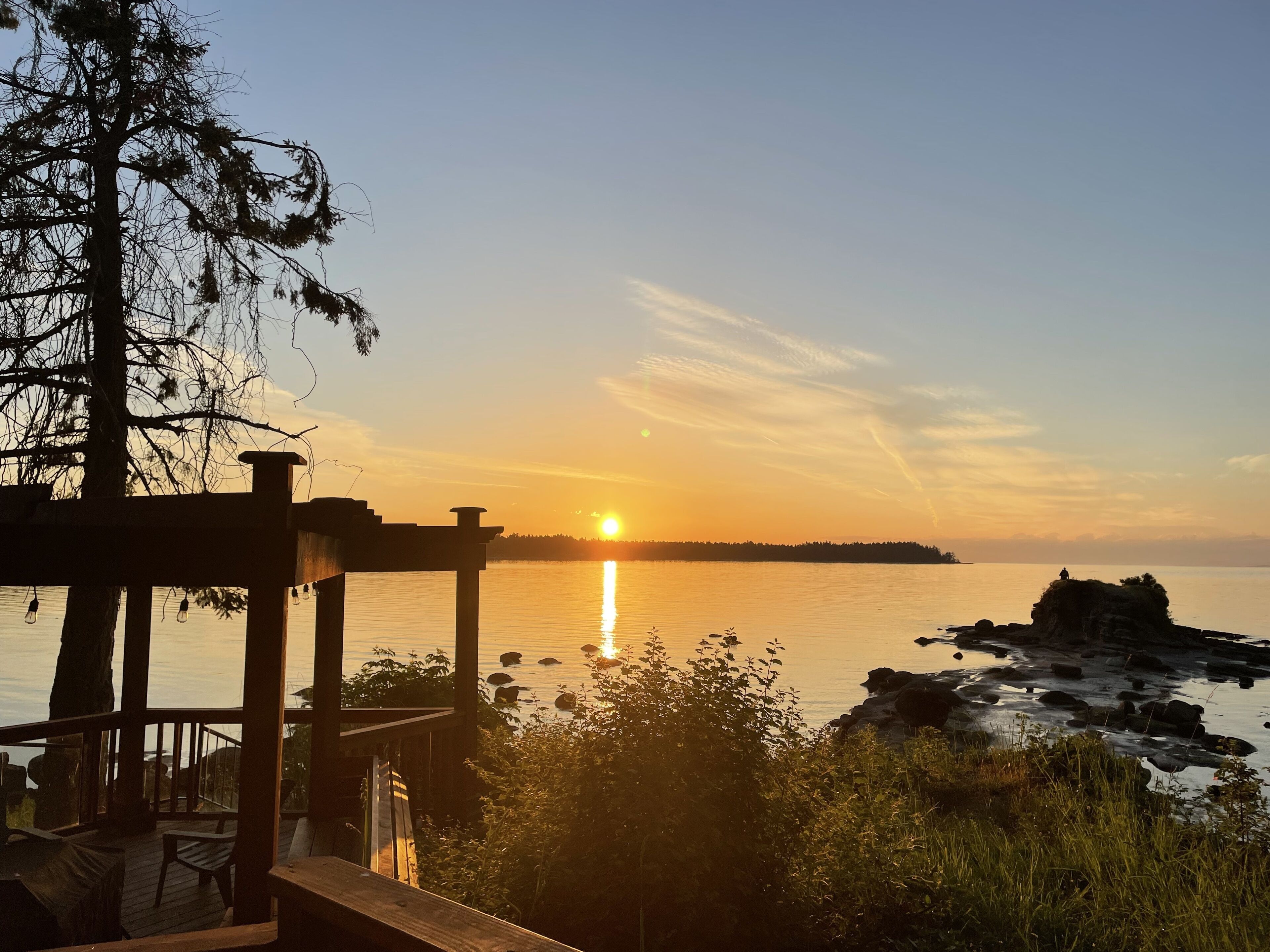 A wooden deck overlooking a calm body of water with a sunset in the background.