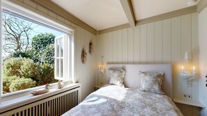 Un dormitorio con una cama grande, una ventana con vistas a la vegetación, un radiador y apliques de pared.