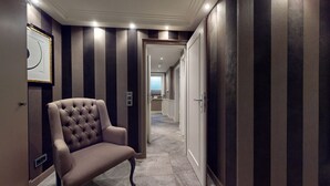 Een gang met een fauteuil met knopen, donkere streepmuren en een deur naar een badkamer.