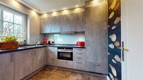A modern kitchen with grey cabinets, a built-in oven, and a window with a view of trees.