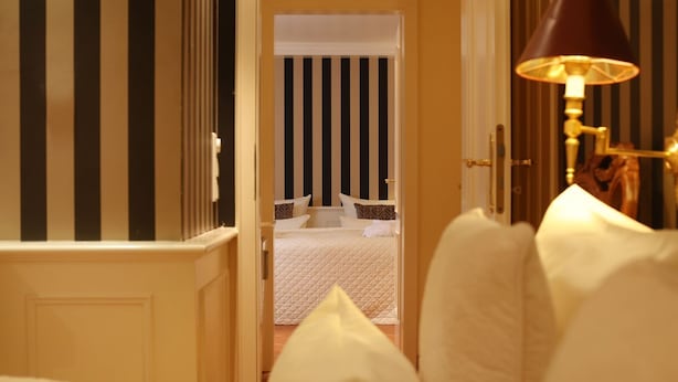Et hotelværelse med en seng, en natlampe og udsigt til en stribet væg og et andet værelse.