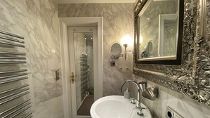 A bathroom with a white sink, a mirror with an ornate frame, and a shower area visible through a glass door.