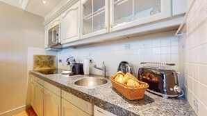 A kitchen with white cabinets, a granite countertop, a toaster, a kettle, and a basket of bread.