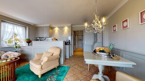 A spacious living room with a beige armchair, a dining table with a fruit bowl, and a chandelier. - Pure Sylt - Exclusive luxury apartment in a quiet location on the Munkmarsch Wadden Sea. (Sylt)