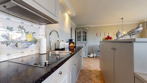 A kitchen with a black countertop, white cabinets, a stainless steel sink, and a decorative backsplash. - Pure Sylt - Exclusive luxury apartment in a quiet location on the Munkmarsch Wadden Sea. (Sylt)