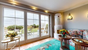 A spacious room with large sliding glass doors leading to a patio, a sofa with floral upholstery, and a decorative vase with flowers. - Pure Sylt - Exclusive luxury apartment in a quiet location on the Munkmarsch Wadden Sea. (Sylt)