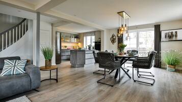 Een moderne keuken met grijze kastjes, een centraal eiland en een eethoek met rieten stoelen en een houten tafel.
