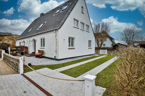 Ein weißes Haus mit geneigtem Dach, einer gepflasterten Auffahrt und einem kleinen Garten.
