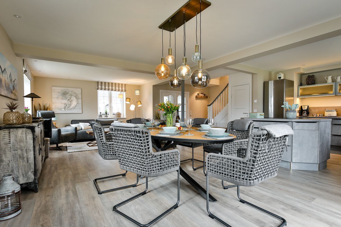 Een moderne keuken met een eethoek, met een groot schiereiland, hanglampen en rieten stoelen.