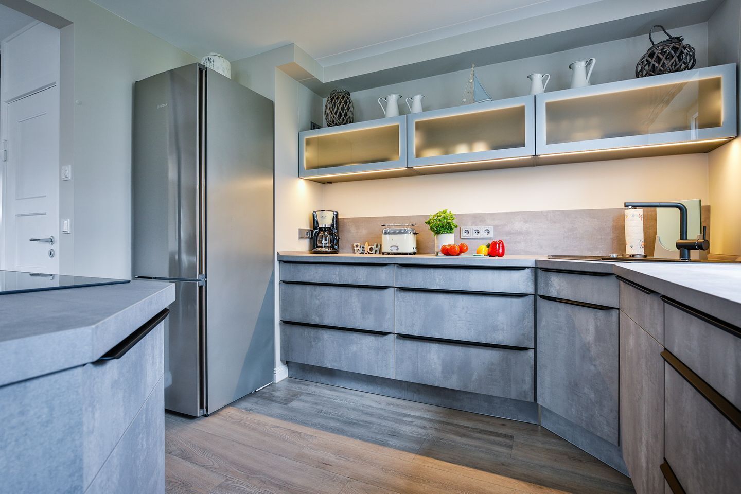 A modern kitchen with a built-in refrigerator, a coffee maker, a toaster, and a sink with a faucet.
