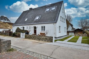 Ein weißes, zweistöckiges Haus mit geneigtem Dach, einer Steinmauer und einem gepflasterten Einfahrtsweg.