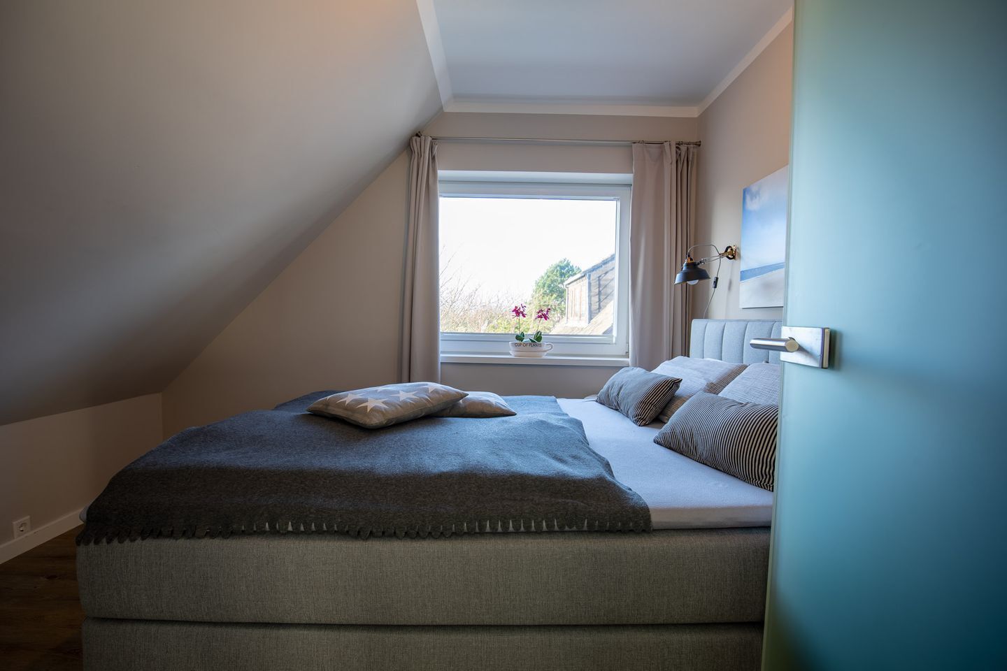 Ein Schlafzimmer mit einem Bett, Kissen, einem Fenster mit Vorhängen, einem Nachttisch und einer Lampe.