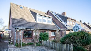 A two-story house with a sloped roof, a visible chimney, and a small garden area with a wooden fence. - Sylt Like - Modernes Appartement in Zentraler Lage für bis zu Zwei Personen (Sylt)