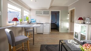 A modern kitchen with a dining area, a small table with chairs, and a view of the city through large windows. - Sylt Like - Modernes Appartement in Zentraler Lage für bis zu Zwei Personen (Sylt)