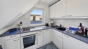 Una cocina moderna con armarios blancos, horno empotrado, un lavamanos y una ventana con vistas a un edificio.