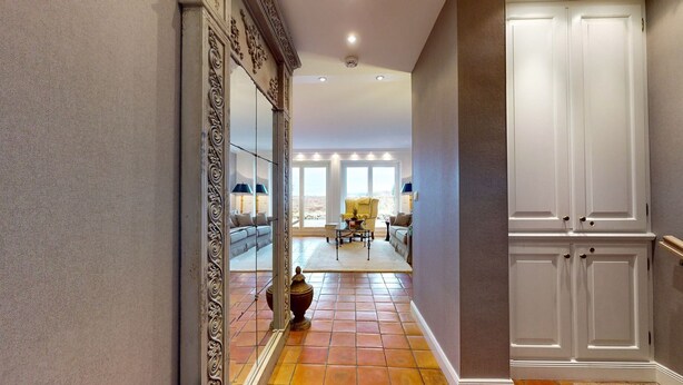 A hallway with a large mirror, a tiled floor, and a view into a living area with a sofa and a table.