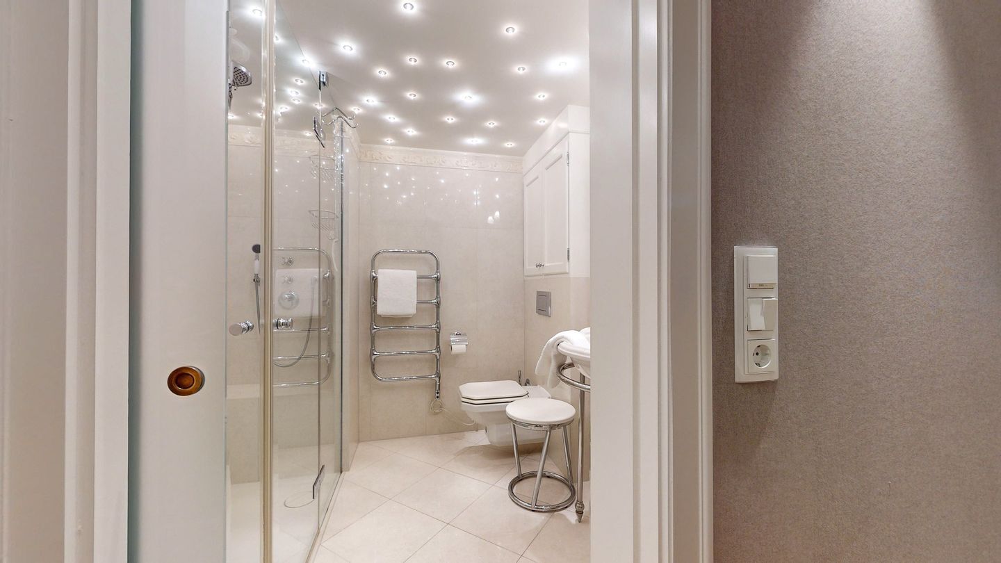 A modern bathroom with a glass shower enclosure, a toilet, and a small stool.