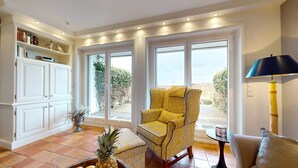 A room with a yellow armchair, a small table, a lamp, and a white cabinet with books.