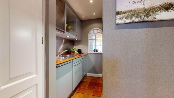 A narrow kitchen with a window, a sink, and a countertop with various items.