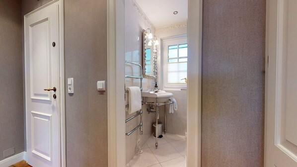 Un couloir étroit mène à une salle de bain avec une porte blanche, un lavabo et un miroir.