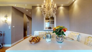 A dining area with a white table set for four, a chandelier, and a vase with flowers.