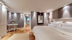 A modern hotel room with a large bed, a bedside table with a vase of flowers, a mirror, and a lamp.